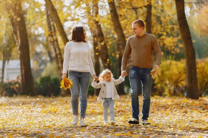 Parents walking through a park with their daughter in autumn.