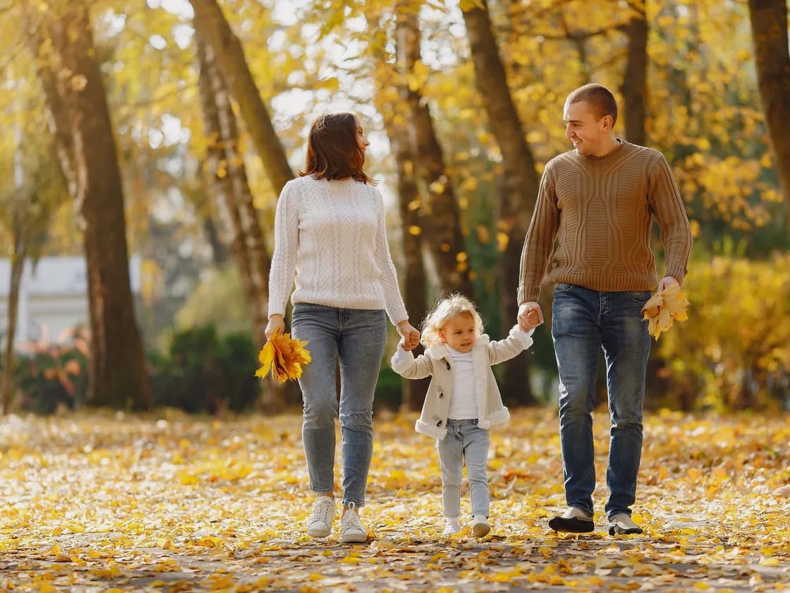 Parents walking through a park with their daughter in autumn.