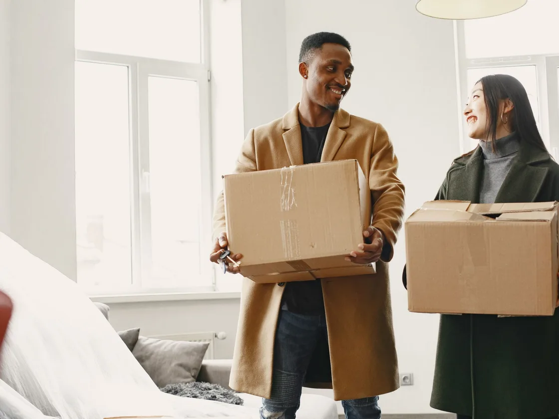 A couple carrying moving boxes into a new home.