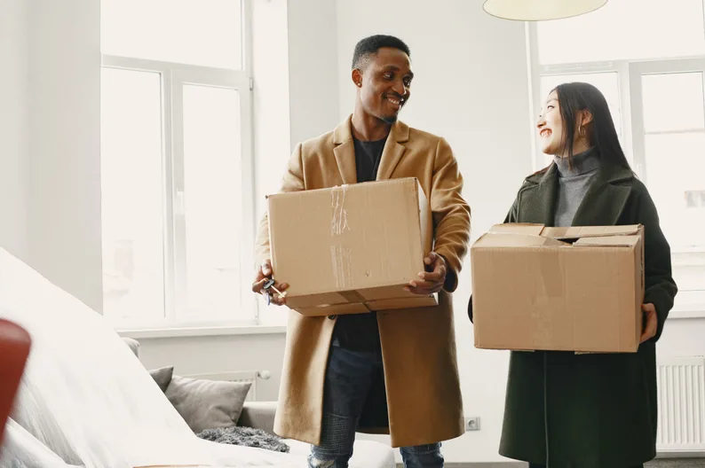 A couple carrying moving boxes into a new home.